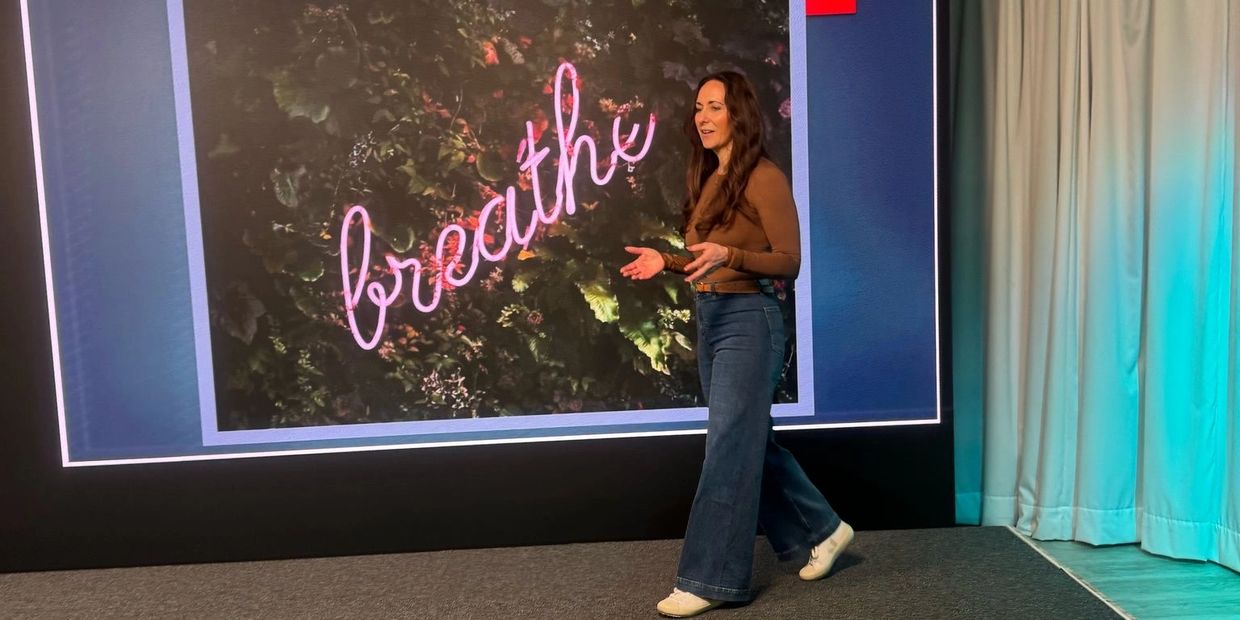 Woman speaking on stage with a 'breathe' sign in pink behind her.