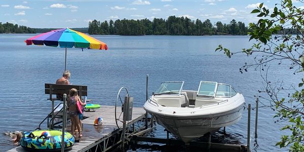 A lakeside dock with a boat, colorful umbrella, and people enjoying a sunny day.