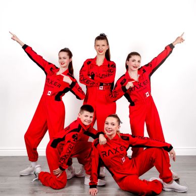 Group of five dancers in red outfits posing confidently.