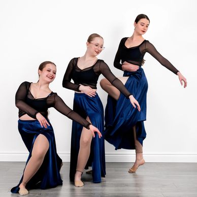 Three ballerinas posing in blue skirts and black tops.