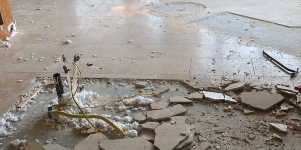 Broken floor tiles and exposed pipes during renovation.