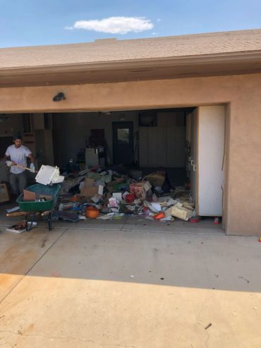 Man cleaning out a garage filled with clutter and trash.