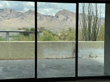 Mountain view through large glass windows with desert vegetation outside.