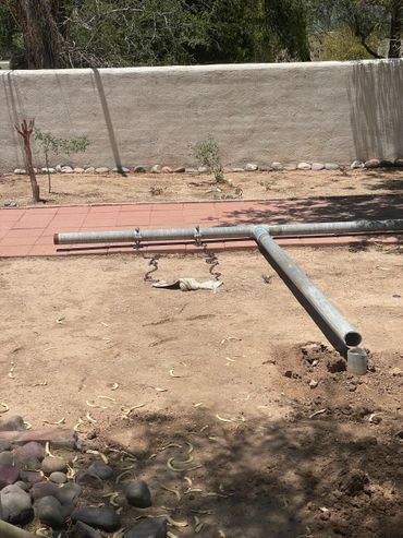 Disassembled metal pipes and a barren yard with a stone border and a bare tree.