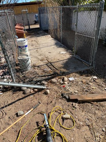 A fenced backyard area with construction materials and tools scattered on the ground.