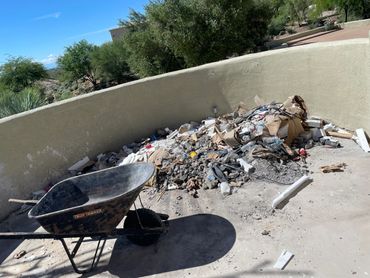 Wheelbarrow near a pile of construction debris and trash outdoors.