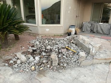 Rubble and debris in a backyard under renovation with covered patio furniture.