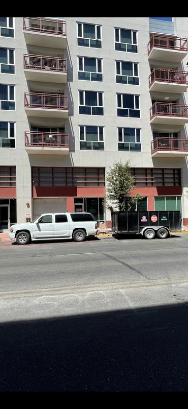 White SUV with black trailer parked in front of an apartment building on a sunny day.