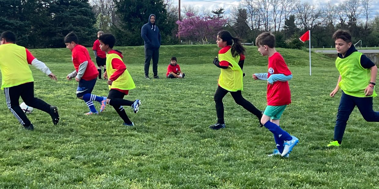 Children playing soccer on a grassy field with a coach watching.