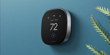 Modern smart thermostat displaying temperature on a blue wall.