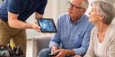 Technician showing smart home controls on a tablet to elderly couple.