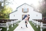 Groom kissing bride in front of white barn ceremony site