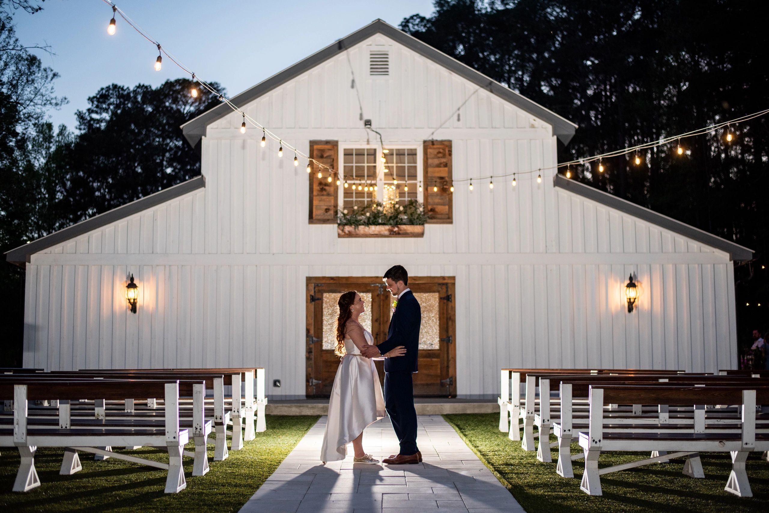 Bride and groom standing in front of a white barn at night