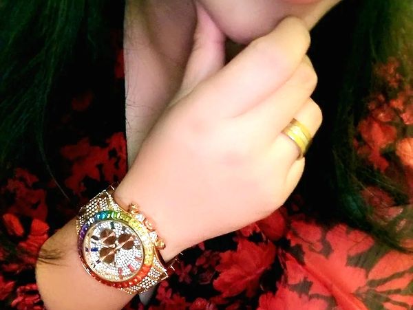Hand with a colorful jeweled watch and gold ring.