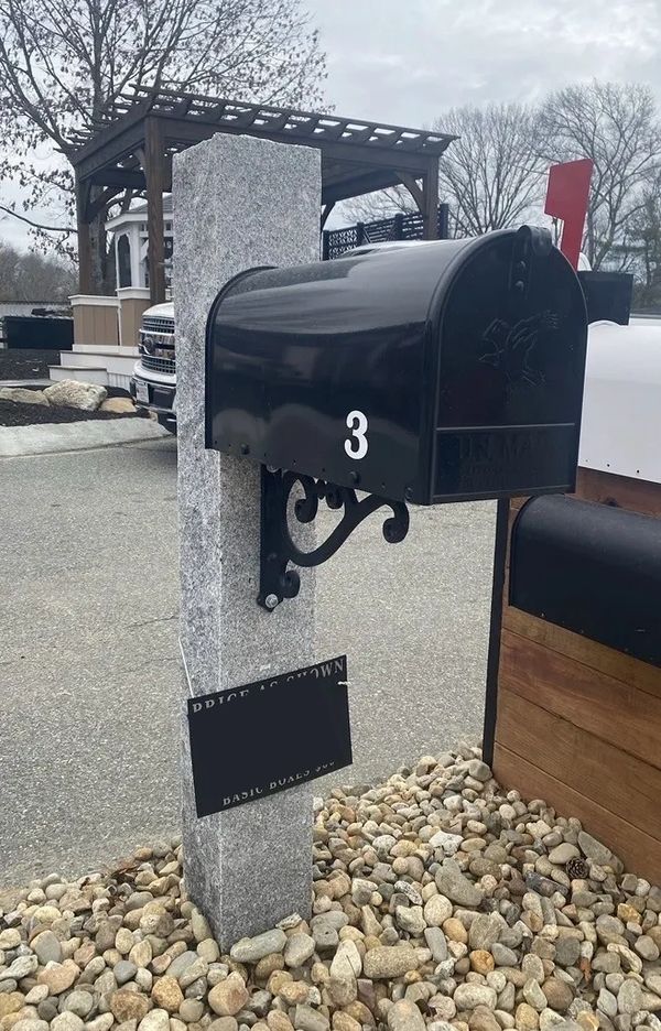 Black mailbox with number 3 on a stone pillar surrounded by rocks.