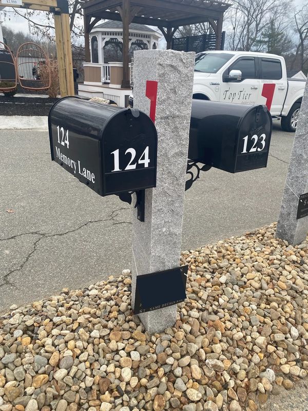 Two black mailboxes numbered 123 and 124 on a stone post with gravel below.