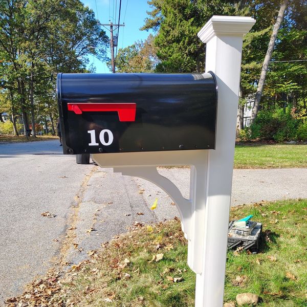 Black mailbox with red flag and number 10 on a white post.