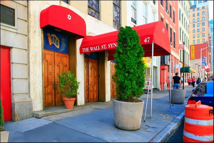 Red awning entrance to The Wall St. Synagogue on a city street.