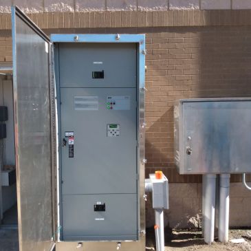 An open electrical control panel box outside a building.