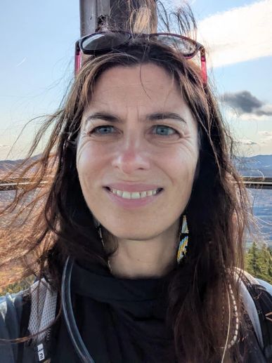 Woman with long hair smiling outdoors with sunglasses on her head.