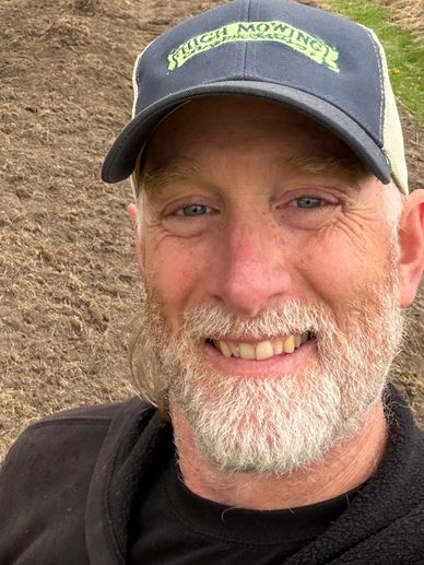 Smiling man with a gray beard wearing a cap outdoors.