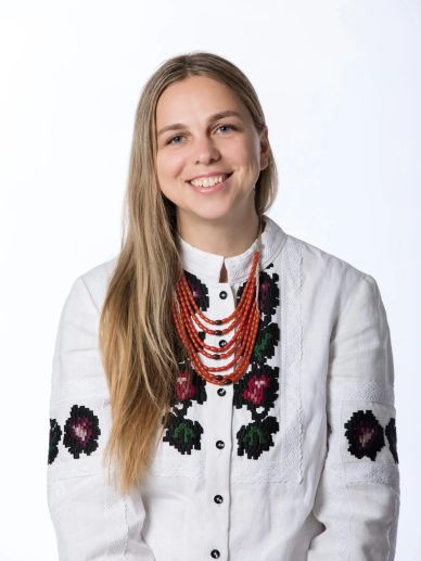 Smiling woman in white traditional embroidered blouse with red beaded necklace.