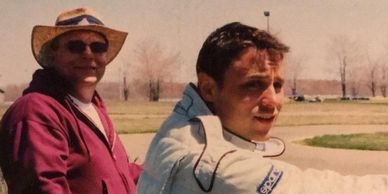 Rob Piekarczyk stands in his driver's suit at a fence next to his father at an SCCA race at Nelson Ledges.