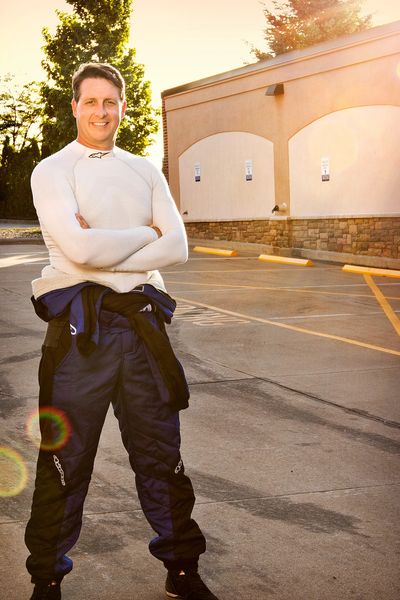 Fritz Wilke stands in his driving suit in front of he Chelsea Michigan Clocktower Complex with the setting sun behind him.  2017.
