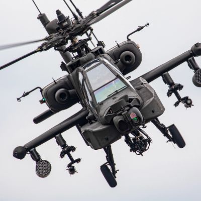 Close-up of an Apache attack helicopter in flight against a cloudy sky.