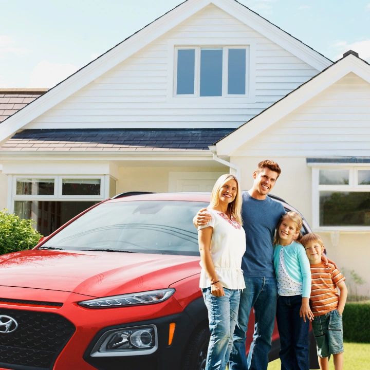 Happy family posing by a red car in front of their house.