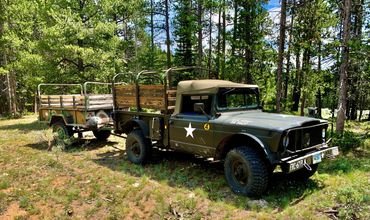 Military-style truck with trailer in a forest clearing.