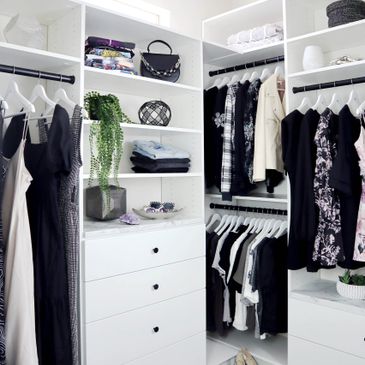 A modern, organized walk-in closet with white shelving and hanging clothes.