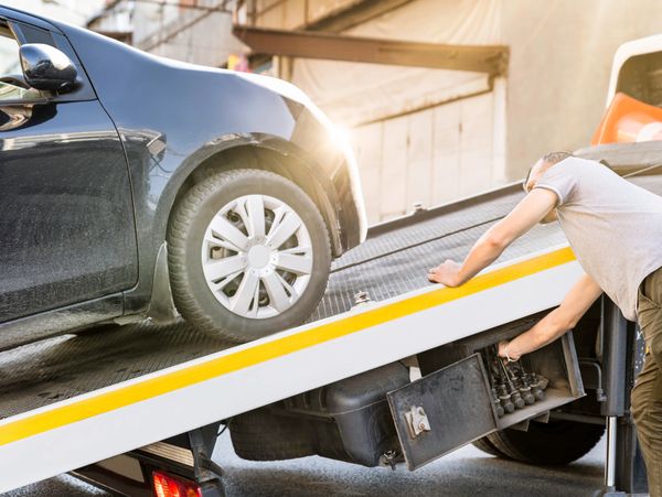 A tow truck driver secures a black car on the ramp of the truck under a warm sunlight