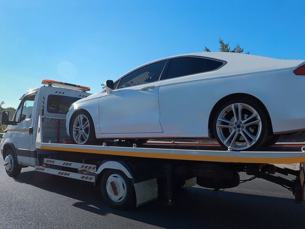 A white car being towed on a flatbed truck under a clear blue sky