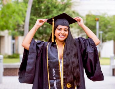 Smiling graduate adjusting her cap outdoors.