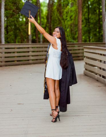 Young woman in white dress with graduation attire smiling outdoors.