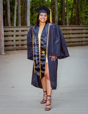 Happy graduate in cap and gown outside.