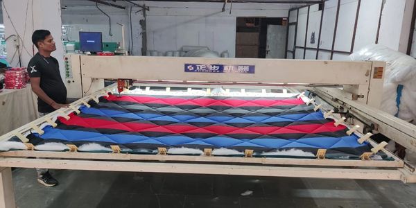 A man operates a quilting machine stitching a colorful fabric pattern.