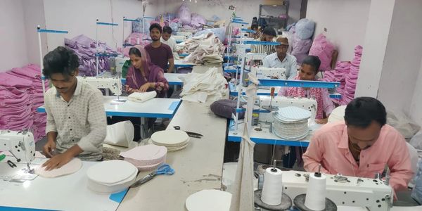 Workers sewing fabric pieces in a textile workshop.