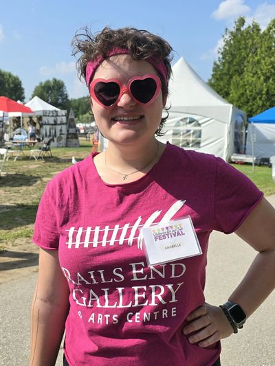 a person with short hair, wearing pink heart shaped glasses and a pink t shirt with the words Rails