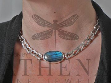 closeup of a woman's neck weating a neclace  made of silver links and a bright blue stone set in sil