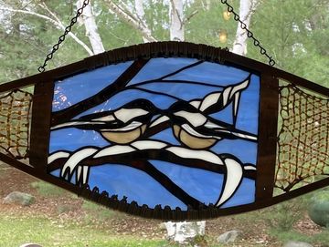 a stained glass images of two chickadees againsta blue background, mounted insit a snowshoe and han