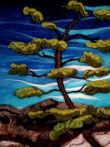 felted wool "painting" of a single windswept pine tree against s a deep blue sky and in the distance