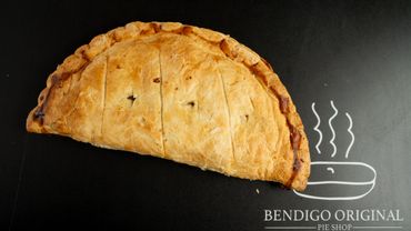 Golden-brown baked pie on a black surface with Bendigo Original Pie Shop logo.