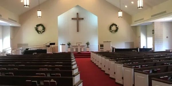 Church interior with wooden pews and a cross at the altar.