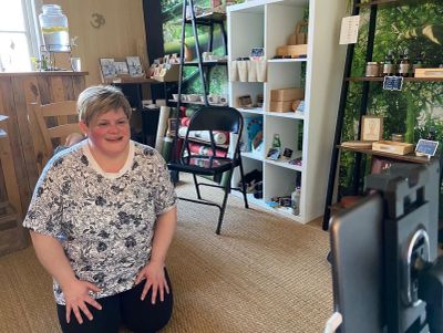 Woman kneeling and smiling in a cozy indoor shop setting.