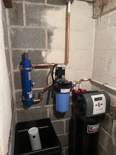 Water softener system installed in a basement with copper piping.
