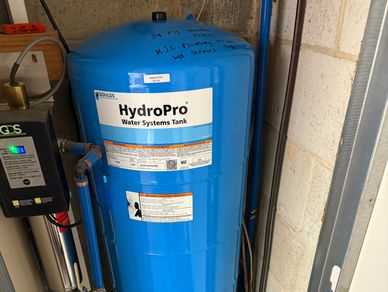 Blue HydroPro water systems tank with warning labels in a utility room.