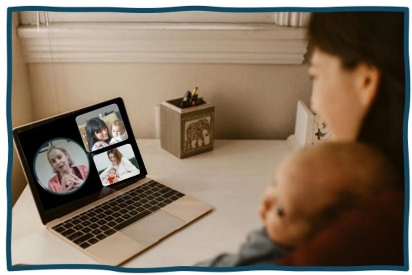 Woman holding baby while on a video call with three people on laptop.