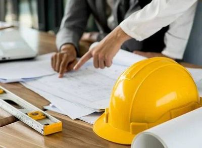 People discussing construction plans at a desk with a yellow hard hat.
